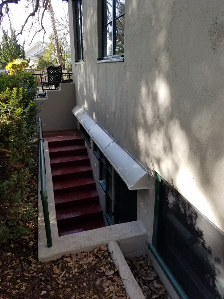 Long DOORBRIM rain guard mounted above a bank of windows in a cellar stair well.