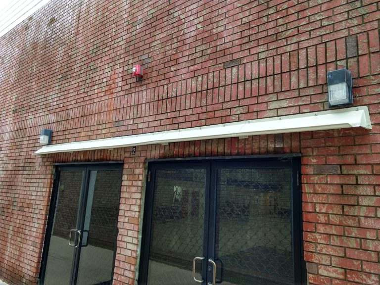 long white DOORBRIM rain diverter installed over 2 bronze sliding glass doors in a brick building.