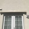 Beige window canopy on second floor above double French doors in beige stucco building.