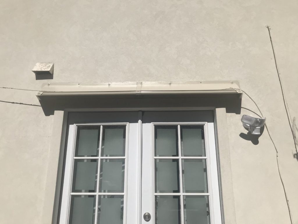 Beige window canopy on second floor above double French doors in beige stucco building.