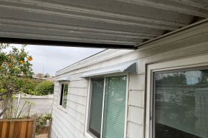Image of gray DOORBRIM rain diverter mounted above a horizontal sliding window in a mobile home with gray lap siding to stop leaks.
