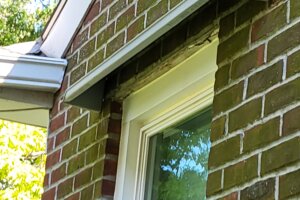 Doorbrim rain diverters mounted above a window in a red brick building.