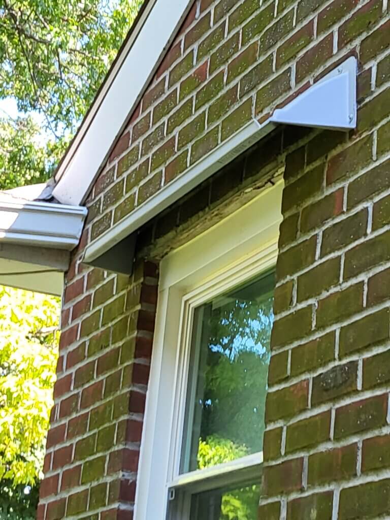 Doorbrim rain diverters mounted above a window in a red brick building.