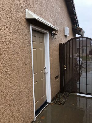Beige DOORBRIM rain diverter mounted above a dark brown entrance door.