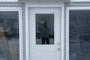 Off white DOORBRIM rain diverter mounted above a porch door with upper half glass and a large window on each side.