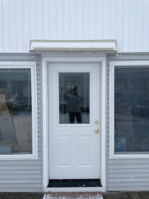 Off white DOORBRIM rain diverter mounted above a porch door with upper half glass and a large window on each side.