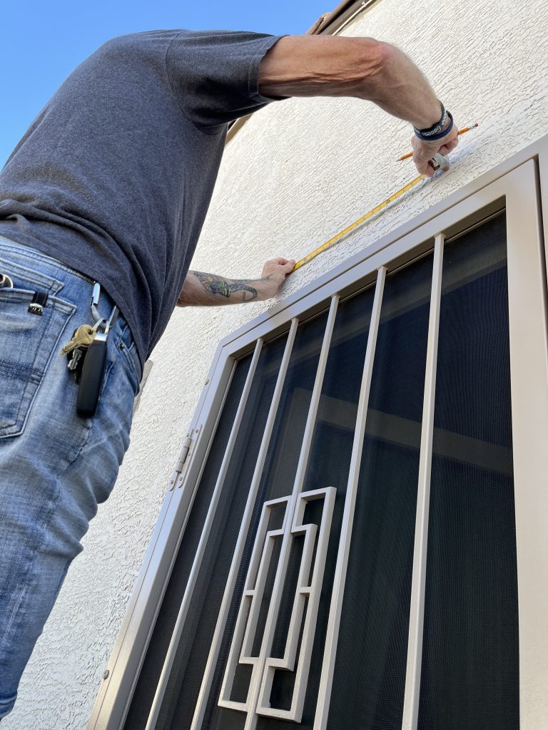 Man measuring over a screen door with vertical bars and center medallion. Getting ready to install a DOORBRIM rain diverter.