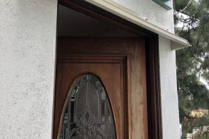 Beige DOORBRIM rain diverter mounted above a dark brown entrance door with an oval glass insert.