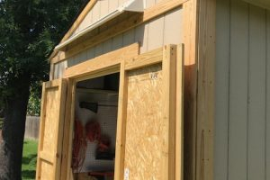 Beige rain guard for shed mounted above double open shed doors. Viewed from right side.