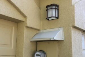 Off-white electric meter cover above meter box in corner of building.