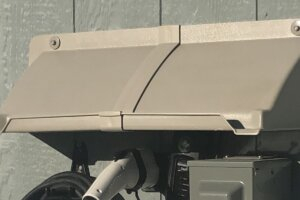 DOORBRIM rain hood installed above an EV charger mounted on T-111 siding.