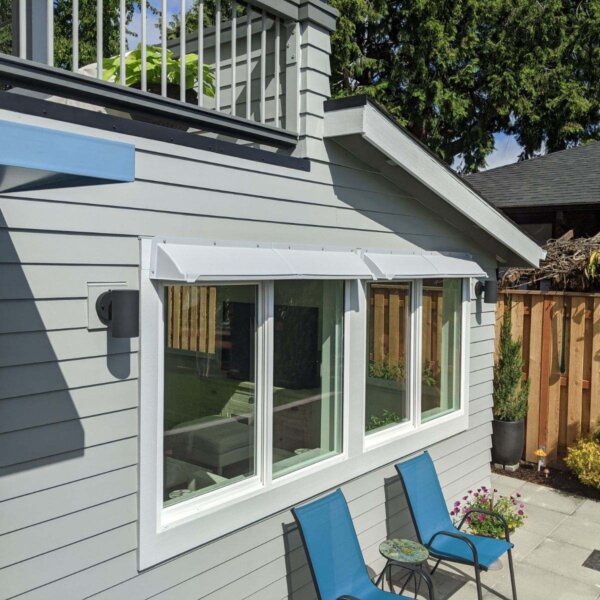 DOORBRIM awning or window rain guard mounted above 2 bay windows on gray siding.