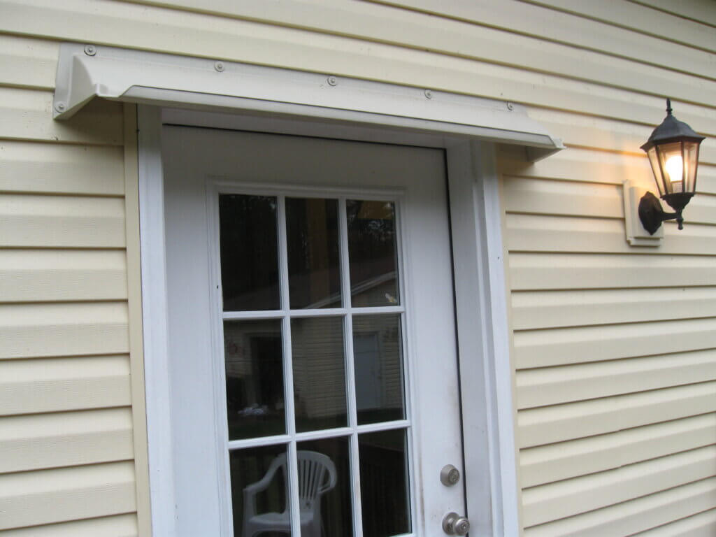 Almond color DOORBRIM awning above 9 lite side door on yellow vinyl siding.